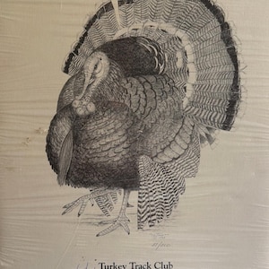 May include: A detailed black and white drawing of a turkey with its tail feathers fanned out. The artwork is signed and includes the text "Turkey Track Club Black Hills, SD 1974-1994". The drawing is on a light-colored background.
