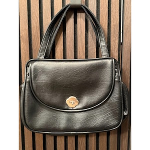 May include: Black leather handbag with a flap closure and top handles. The bag features a gold-colored clasp with a floral design. The bag has a structured shape and appears to be vintage.