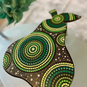 Puede incluir: Una bandeja de servir de madera con forma de pera pintada con puntos verdes, amarillos y negros en un patrón circular.
