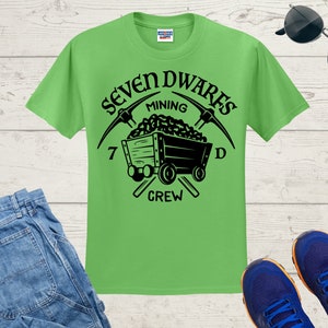 May include: A green t-shirt featuring a black graphic of a mining cart and pickaxes. The text "Seven Dwarves Mining Crew" is printed on the shirt.