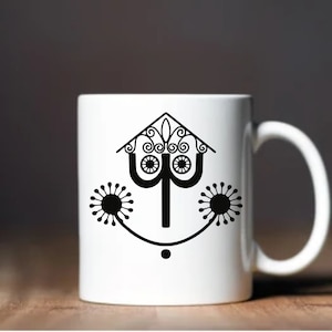 May include: White ceramic mug with a black silhouette of a stylized house with a whimsical design. The house has a pointed roof with a decorative finial and two stylized flowers on either side.