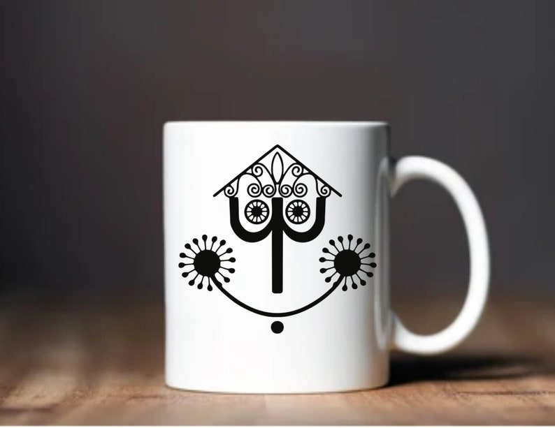 May include: White ceramic mug with a black silhouette of a stylized house with a whimsical design. The house has a pointed roof with a decorative finial and two stylized flowers on either side.