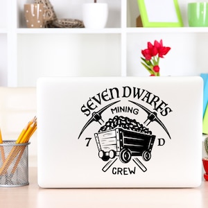 May include: A black and white laptop sticker with the text "Seven Dwarves Mining Crew" and a cartoon image of a mine cart filled with coal and two pickaxes crossed behind it.
