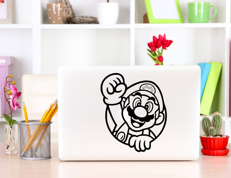 K&ouml;nnte beinhalten: Ein schwarz-wei&szlig;er Aufkleber von Mario, einer Videospielfigur, auf einem wei&szlig;en Laptop. Mario tr&auml;gt einen Hut und einen Schnurrbart. Er h&auml;lt seine Faust in die Luft.