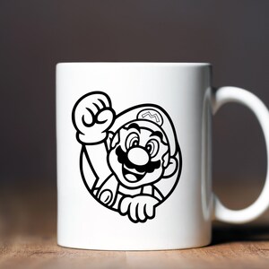 K&ouml;nnte beinhalten: Eine wei&szlig;e Keramiktasse mit einer Schwarzwei&szlig;illustration von Mario aus der Super Mario Bros. Videospielserie. Mario tr&auml;gt seine charakteristische rote M&uuml;tze und Latzhose und macht mit seiner rechten Hand eine Faust.