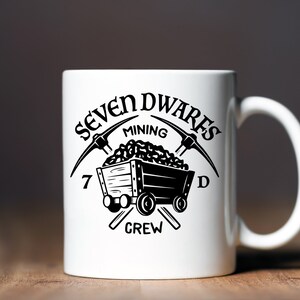 May include: White ceramic mug with a black graphic of a mining cart filled with coal and two crossed pickaxes. The text "Seven Dwarfs Mining Crew" surrounds the graphic.