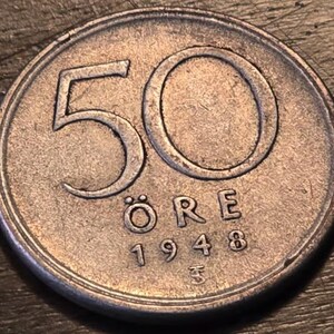 Könnte beinhalten: Nahaufnahme einer schwedischen 50-Öre-Münze von 1948. Die Münze hat eine stumpfe Silberfarbe und zeigt die Zahl "50" in großer Schrift, zusammen mit dem Wort "ÖRE" und dem Jahr "1948".