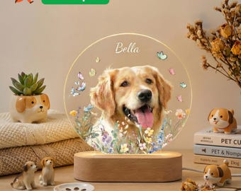 Pode incluir: Uma luz noturna personalizada com retrato de cão e o nome "Bella" numa base de madeira. A luz apresenta uma imagem de golden retriever rodeada por flores e borboletas. Decoração canina adicional.