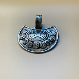 May include: A silver pendant with a crescent moon shape and a detailed design of concentric circles and spirals.
