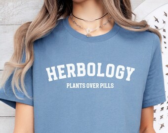May include: A light blue t-shirt with the text "HERBOLOGY PLANTS OVER PILLS" in white.