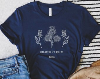 May include: A navy blue t-shirt with a white graphic of a burdock plant and the text "Herbs are the best medicine, Burdock".