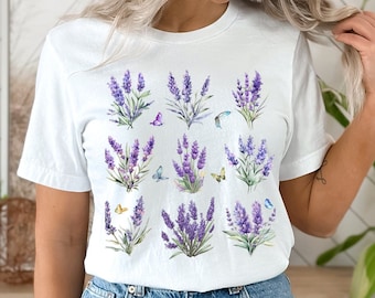 May include: White t-shirt with a lavender floral print and butterflies. The shirt features a repeating pattern of lavender flowers and butterflies in shades of purple, blue, and yellow.