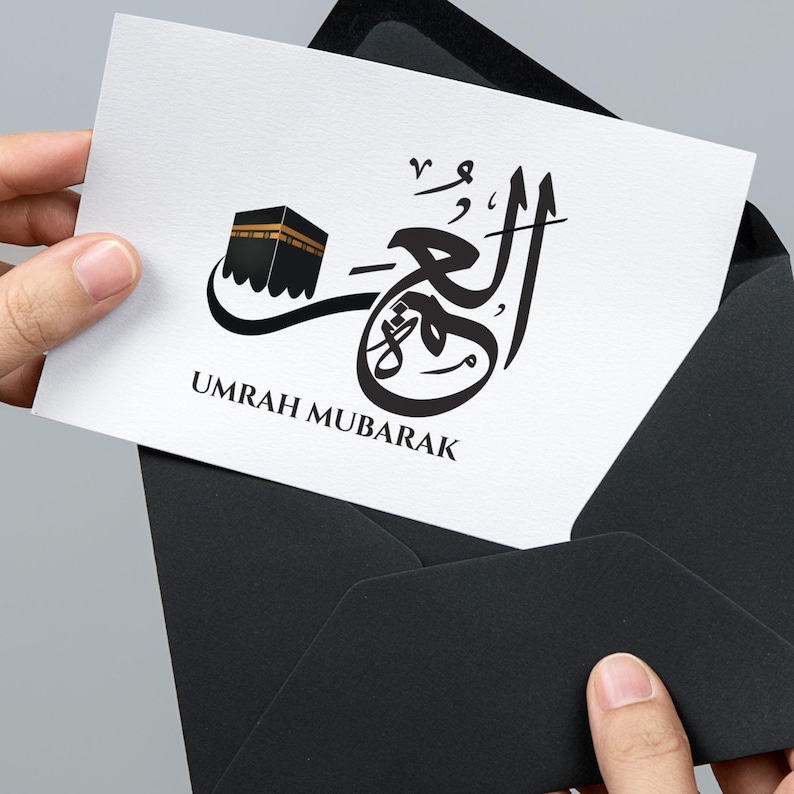 May include: A white card with black calligraphy that says "Umrah Mubarak" and a black and gold illustration of the Kaaba.