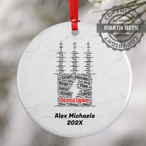 May include: White round ceramic ornament with a black word cloud in the shape of a stylized electrical tower. The word cloud includes terms related to electrical engineering, such as circuits, electronics, design, control, systems, power, and energy. The ornament is personalized with the name "Alex Michaels" and the year "202X" in red text.