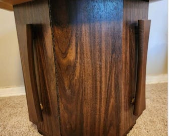 May include: A dark brown octagonal wooden side table with two long, narrow, vertical wooden handles on the front. The table has a smooth, polished finish.