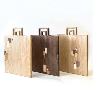 May include: Three wooden chopping boards with handles. The boards are made from different types of wood, including oak and walnut. The handles are made from the same wood as the boards. The boards are all the same size and shape.
