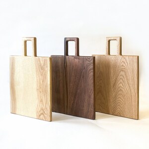 May include: Three wooden chopping boards with handles. The boards are made from different types of wood, including light wood and dark wood.