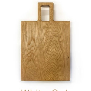 May include: A rectangular wooden chopping board made of white oak with a handle. The handle has a rectangular cutout.