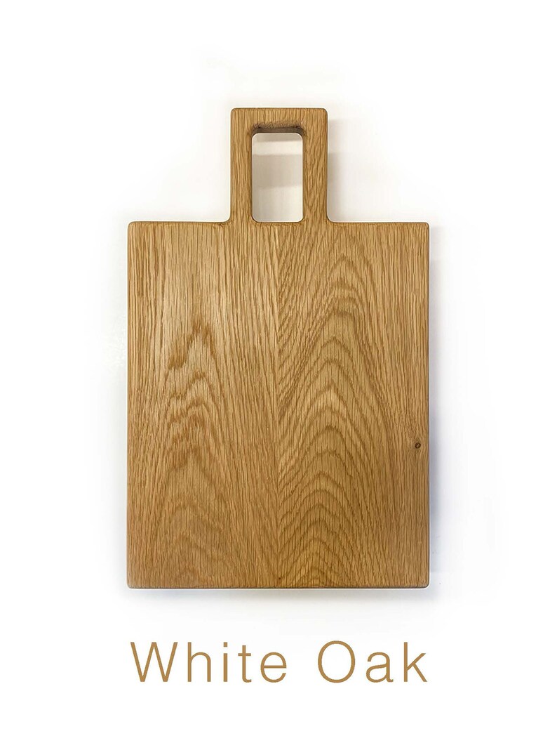 May include: A rectangular wooden chopping board made of white oak with a handle. The handle has a rectangular cutout.