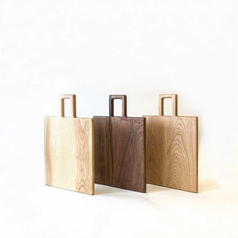 May include: Three wooden chopping boards with handles. The boards are made from different types of wood, including light wood and dark wood.