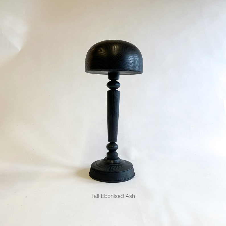 Op de afbeelding: Een hoge zwarte houten hoedenstandaard met een ronde bovenkant en een voet. De standaard is gemaakt van ge&euml;boniseerde essenhout. "Tall Ebonised Ash" staat onder de standaard.