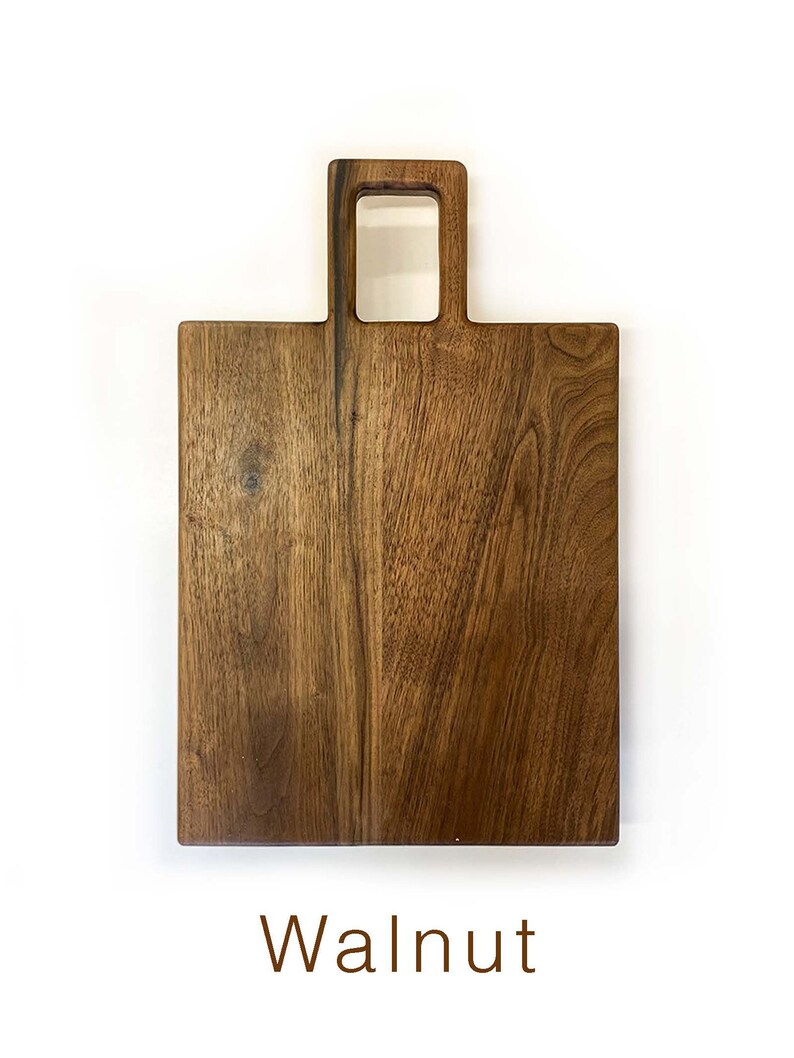 May include: A rectangular walnut wood chopping board with a handle. The handle has a square opening in the centre.