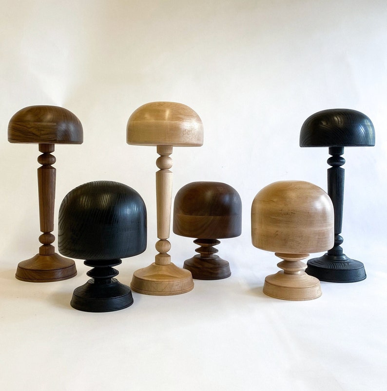 Op de afbeelding: Zes houten hoedvormen in verschillende kleuren en stijlen. De vormen zijn gemaakt van hout en hebben een gladde afwerking. Ze zijn allemaal van verschillende grootte en vorm.