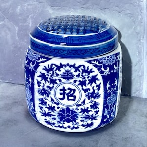 May include: A blue and white ceramic jar with a floral design and a circular top with a grid pattern. The jar has a round shape and features a Chinese character in the center.