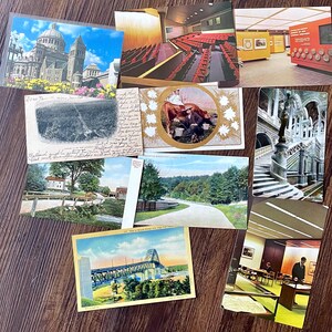 May include: A collection of vintage postcards featuring various scenes. The postcards depict a cathedral, a theater, a bridge, a road, a farm, and a man with a cow. The postcards are in various colors, including blue, green, and brown.
