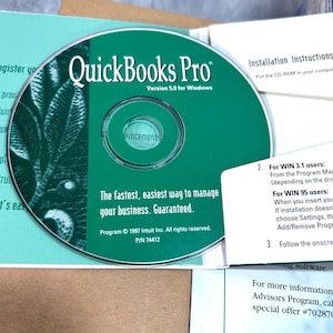 Könnte beinhalten: Eine grüne QuickBooks Pro Version 5.0 für Windows Software-CD. Die Disc enthält weißen Text mit der Aufschrift The fastest, easiest way to manage your business. Guaranteed. Program 1997 Intuit Inc. All rights reserved. P/N 74412 und Annoucements.