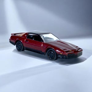 May include: A miniature burgundy sports car with a black roof and black wheels. The car has a sleek design with a low profile and a detailed front end. The car is a classic model.