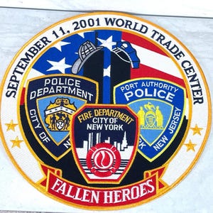 Peut inclure: Écusson brodé commémorant les attentats du World Trade Center du 11 septembre 2001. Comprend le drapeau américain, les tours jumelles et les emblèmes des services de police et d'incendie. Le texte comprend "Fallen Heroes".