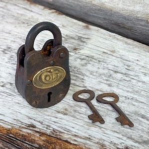 Op de afbeelding: Een vintage, roestig hangslot met een messing plaatje met de tekst "OLT" en twee bijpassende sleutels. Het slot is donkerbruin met een gebogen beugel. De sleutels zijn ook roestbruin.