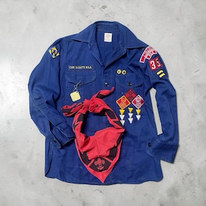 May include: A vintage blue Cub Scouts B.S.A. uniform shirt with patches and a red neckerchief. The shirt has the text "CUB SCOUTS B.S.A." and a "Lincoln New Jersey 35" patch. The red neckerchief has a black border and a fleur-de-lis emblem.