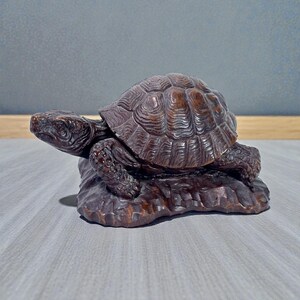 May include: A detailed, brown wooden turtle figurine. The turtle has a textured shell and is perched on a carved base. The figurine is a decorative item, likely for display.