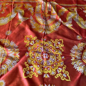 May include: A red textile with intricate gold and silver embroidery. The design features stylized birds, floral patterns, and sunburst motifs. The top edge has a fringe of red threads. The fabric has a lustrous sheen.