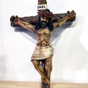 May include: A handcrafted wooden crucifix sculpture depicting Jesus Christ. The figure has a crown of thorns, a loincloth, and visible wounds. The cross has the inscription "INRI" on a white banner.