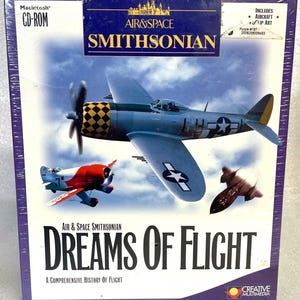 May include: A CD-ROM box for "Air & Space Smithsonian: Dreams of Flight." The cover features illustrations of various aircraft, including a blue and gray fighter plane with a checkered pattern on the tail, and the text "Dreams of Flight."