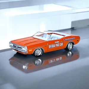 May include: An orange Dodge Challenger convertible model car. The car has white interior and the text "Dodge OFFICIAL PACE CAR" on the side. The car is a miniature replica of the 1970s model.