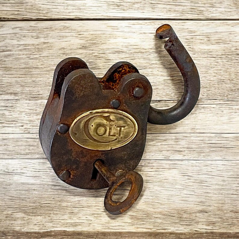 Op de afbeelding: Een antiek, roestig hangslot met een sleutel. Het slot is donkerbruin met een messing plaatje met de tekst "COLT". De sleutel is ook roestig. De beugel van het slot is open.