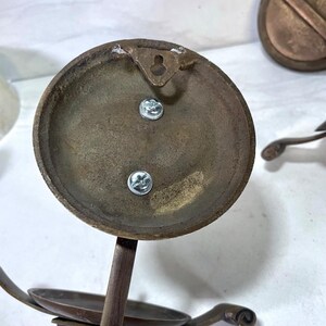 May include: Close-up of antique brass candle holders. The candle holders have a circular base with a small dish for the candle and decorative curved arms. The back of the base has a keyhole for hanging and two screws.