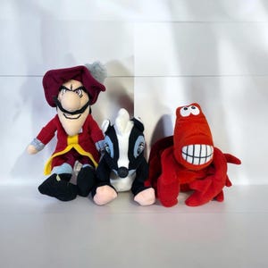 May include: Three plush toys: a red-coated pirate with a mustache, a black and white skunk, and a red crab with a large, toothy grin. The toys are soft and colorful, perfect for children or collectors.