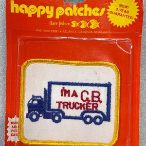 Könnte beinhalten: Ein Vintage-Patch "I'M A C.B. TRUCKER" mit einem blauen LKW-Design auf weißem Hintergrund, umrahmt von einem gelben Rand. Der Patch ist in einer roten Plastikkarte verpackt. Die Verpackung enthält den Text "happy patches".