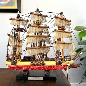 May include: A detailed model of the clipper ship "Sea Witch" from 1846. The ship features tan sails, wooden masts, and a red hull. The model is displayed on a black base with the ship's name and year.