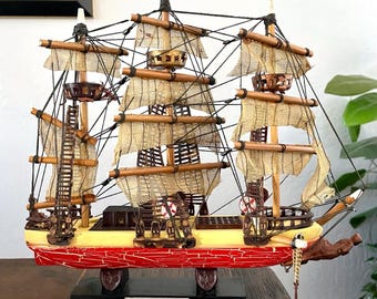 May include: A detailed model of the clipper ship "Sea Witch" from 1846. The ship features tan sails, wooden masts, and a red hull. The model is displayed on a black base with the ship's name and year.
