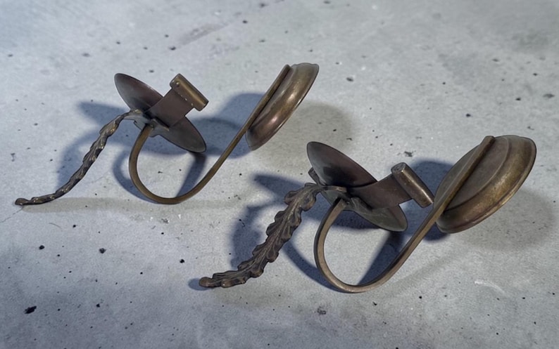 May include: Two bronze-toned earrings. Each earring features a circular disc, a rectangular bar, and a curved, open ring design. One earring has a twisted stem, while the other has a leaf-like stem.