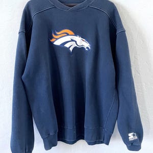 Könnte beinhalten: Marineblaues Sweatshirt mit dem Logo der Denver Broncos auf der Vorderseite. Das Logo ist ein weißer, orangefarbener und blauer Pferdekopf. Das Sweatshirt hat einen V-Ausschnitt und das Starter-Logo auf dem Ärmel.