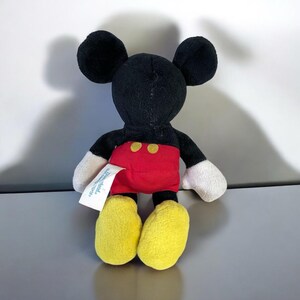 Puede incluir: Un peque&ntilde;o peluche de Mickey Mouse. El juguete tiene cabeza y orejas negras, pantalones cortos rojos con dos botones amarillos, pies amarillos y guantes blancos. Una etiqueta blanca est&aacute; adherida al juguete.