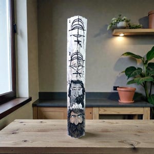 May include: A tall, carved wooden sculpture with four painted faces and the numbers 1-4. The faces are in black and white, with detailed beards and expressions. The wood has a natural, light color.