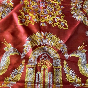 May include: Red fabric with gold, silver, and yellow embroidered patterns. The design includes floral motifs, archways, and deer-like creatures. The fabric has a shiny, textured appearance.